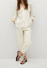 Kermansävyinen paita, jossa napitus ja teksturoidut pilkut, yhdistetty rentoihin norsunluunvärisiin housuihin ja mustiin remmijalkineisiin.