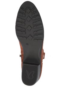 Suela de zapato de gamuza marrón con goma negra texturizada para agarre. Presenta un tacón bajo y un logotipo de mariposa en relieve, además de un detalle superior cosido.