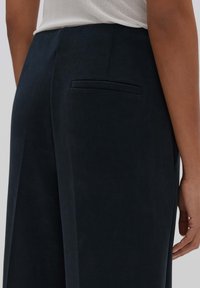 Pantalons taille haute bleu marine foncé avec une texture lisse, dotés d'une poche arrière unique et de coutures subtiles le long des coutures latérales.