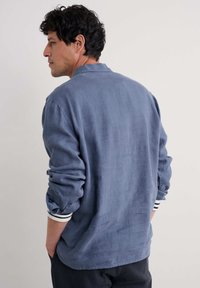 Sininen pellavapaita pitkillä hihoilla, jossa on rento kaulus ja raidalliset hihansuut. Pehmeä kangas ja rento malli, sopii arkikäyttöön.