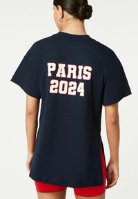 Tricou navy, croi lejer, cu un text îndrăzneț alb „PARIS 2024” și un tiv cu slituri pe laterale. Fabricat din bumbac moale.