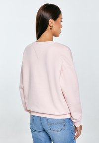 Jasnoróżowy sweter z okrągłym dekoltem, z opadającymi ramionami i ściągaczami przy mankietach. Miękka tekstura, luźny krój i czysty design bez zdobień.