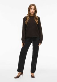 Brązowy sweter z teksturowanej dzianiny, z długimi rękawami, zestawiony z czarnymi spodniami o prostym kroju i brązowymi butami na obcasie, na jednolitym białym tle.