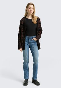 Brązowy i czarny sweter z wzorem noszony na czarnym topie, w połączeniu z niebieskimi dżinsami i czarnymi botkami na platformie. Miękka tekstura, otwarty przód.