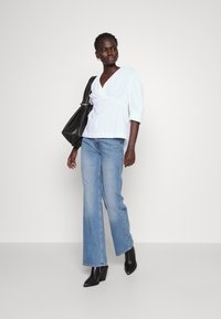 Hvit omslagsbluse med vertikale striper, kombinert med lyseblå straight-leg jeans og svarte hælede ankelstøvler, supplert med en svart tote bag.