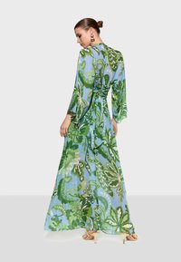 Long, flowing dress in light blue with green floral patterns. Features wide sleeves and a waist tie. Made of sheer, lightweight fabric.