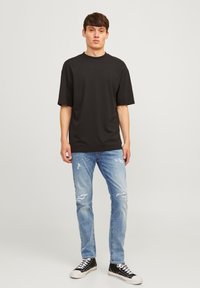 Camiseta corta de algodón negra combinada con jeans desgastados de color azul claro y zapatillas de lona negras con suelas blancas.