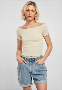 Krämfärgad av-axeln ribbad topp som kombineras med ljusblå denimshorts. Shortsen har upprullade fållar och framfickor.