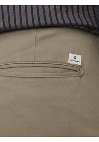 Pantalon en tissu beige avec une poche arrière ornée d'une étiquette cousue. Le matériau est lisse avec une légère brillance et des coutures nettes.