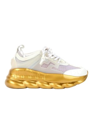 Biały i przezroczysty sneaker z białymi sznurówkami i masywną, metaliczną złotą podeszwą z geometrycznym wzorem.