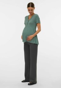 T-shirt de maternité vert clair, à côtes, avec des manches courtes et un col en V, associé à un pantalon large gris foncé et des ballerines noires.