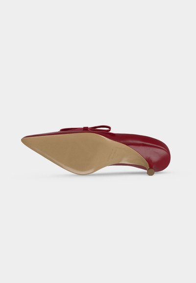 Chaussure à talon haut en cuir rouge avec bout pointu vue de dessous, montrant la semelle beige et la petite pointe du talon.