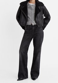 Black faux leather moto jacket with shearling collar, gray button-up cardigan, and high-waisted black wide-leg jeans. Textured materials are visible.