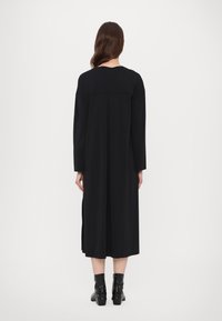 Black long-sleeve dress with a straight cut, mid-calf length, and back pleat detail, paired with black ankle boots featuring silver accents.