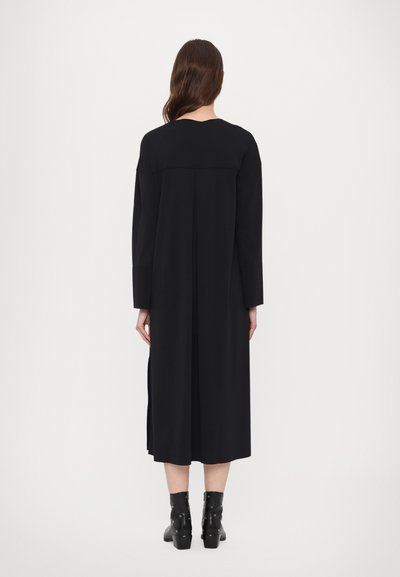 Crna haljina dugih rukava ravnog kroja, do sredine lista, s detaljem na zadnjem dijelu u obliku plisa, uparen s crnim čizmama do gležnja sa srebrnim detaljima.