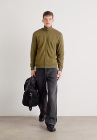 Alyvuogių žalios spalvos užtrauktukas striukė, tamsiai pilkos plačios kojų džinsai, juoda rankinė ir batai. Sklandus paviršius, paprastas dizainas, minimalūs akcentai.