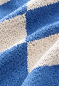 Gros plan sur un tissu tricoté avec un motif en losanges bleu et blanc cassé et une texture de tricot visible.