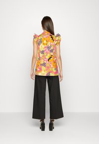 Floral top in pink, orange, and yellow with ruffled sleeves; paired with black wide-leg trousers and heeled sandals.