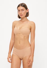 Beige lingerie set featuring a smooth, molded bra with thin straps and matching seamless hipster briefs, crafted from stretchy fabric.