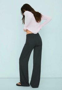 Crne hlače širokih nogavica s krojem po mjeri, uparene s dugim rukavima u svijetlo ružičastoj boji s rebrastim uzorkom, stilizirane s crnim ravnim sandalama.