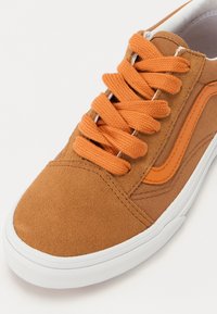 Baskets en suède marron avec des lacets et des accents latéraux orange. Elles présentent une semelle en caoutchouc blanc et des détails cousus. Bout rond, design bas.
