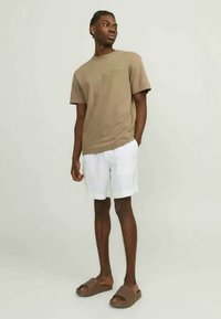 Tan cotton t-shirt with short sleeves, white checkered shorts, and brown slide sandals. Straight fit and casual design.