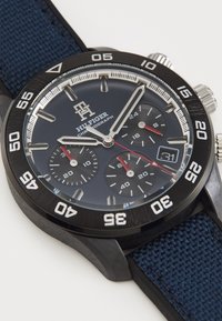Montre chronographe avec un bracelet en tissu bleu marine, un boîtier noir, un cadran bleu foncé, des accents en argent, des index des heures blancs et un affichage de date.