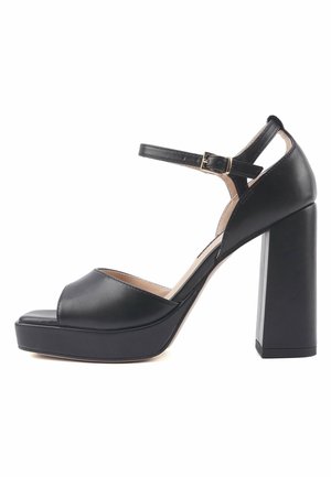 Scarpe platform in pelle nera con design a punta aperta, cinturino alla caviglia e tacco spesso e quadrato. Texture liscia con hardware dorato sul cinturino.