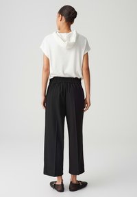 White short-sleeve hoodie with a hood, paired with black wide-leg pants featuring an elastic waist and a side pocket. Black mesh slip-on shoes.