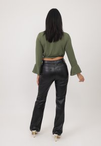 Top corto verde oliva con maniche a campana abbinato a pantaloni in pelle nera a vita alta; texture liscia e design aderente.
