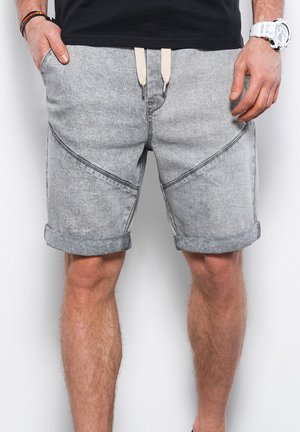 Pantaloni shorts in denim grigio con una superficie texturizzata, dotati di risvolti, cuciture angolate e lacci beige. Inclusi due tasche laterali.