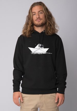 Haut à capuche noir avec une poche avant et un cordon de serrage. Présente un graphique blanc d'un bateau en papier et d'un astronaute dans l'espace. Matériau en coton.