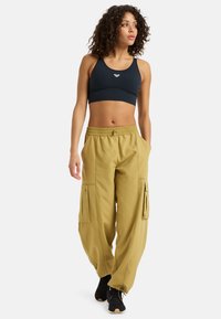 Reggiseno sportivo nero con logo bianco; pantaloni cargo larghi color kaki con grandi tasche laterali e cintura elastica; indossati con sneakers nere.