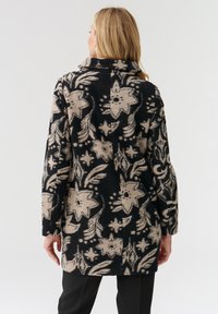 Abrigo de flores en negro y beige con un alto cuello, mangas largas y corte recto, hecho de tela texturizada.