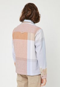 Giacca camicia patchwork in colori pastello; presenta un colletto e polsini con bottone; texture morbida con distintivi blocchi di colore in tonalità chiare.