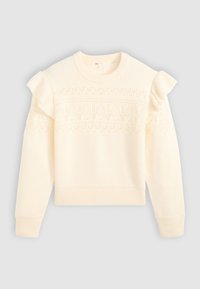 Pull en tricot crème avec un col rond, des manches à volants décoratives et des motifs ajourés au niveau de la poitrine et des épaules.