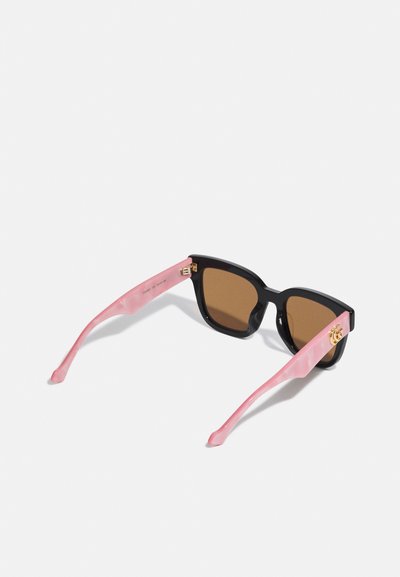 Lunettes de soleil carrées avec des montures noires et des verres marron. Les branches sont roses avec une finition brillante, présentant un détail en accent doré.