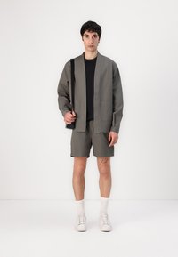 Grå lett jakke med to lommer, kombinert med matchende shorts. Modellen har på seg en svart skjorte og hvite sneakers med ribbet sokker.