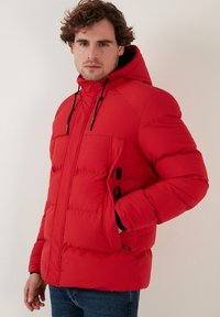 Rød dunjakke med hætte, lavet af et glat, struktureret stof, med frontlynlås og lommer, designet til varme og komfort.