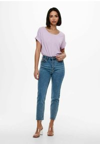 Top corto a maniche corte color lavanda chiaro abbinato a jeans azzurri a vita alta. La modella indossa tacchi trasparenti a blocco con vestibilità dritta e orlo sfrangiato.