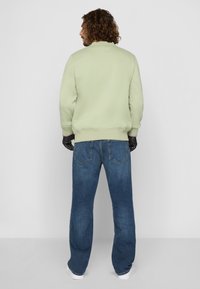 Grønn sweatshirt med ribbestrikkede mansjetter, avslappet passform, kombinert med blå jeans med klassisk fem-lomme-design og subtil falming.