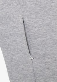 Tela de sudadera gris con una textura suave que presenta un detalle de cremallera lateral en blanco. El material parece suave y ligeramente grueso.