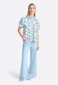 Floral short-sleeve blouse in soft fabric, featuring a light blue base with green and purple flowers, paired with wide-leg light denim pants.