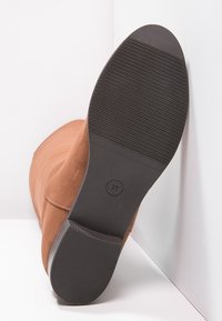 Bottine en daim marron avec un bout arrondi et une semelle en caoutchouc noir texturée. Taille 37 imprimée sous la semelle.