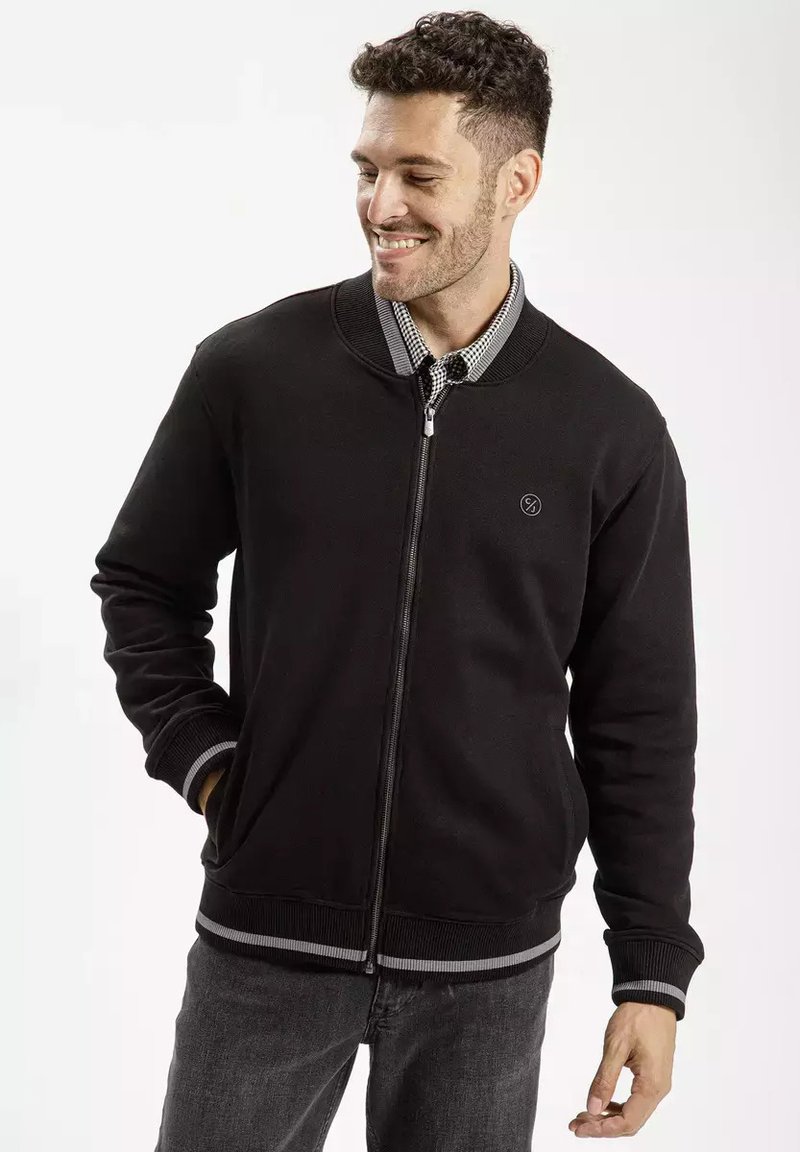 Czarna kurtka zapinana na zamek błyskawiczny z prążkowanym kołnierzem i mankietami, z dyskretnym logo na klatce piersiowej i paskowanymi akcentami na dole.
