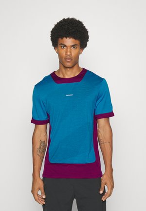 Camisa de manga corta en azul brillante con acentos en púrpura profundo. Tejido texturizado, corte recto y logo en la parte frontal.