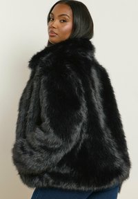 Svart jacka i fuskpäls med en lös passform, hög krage och mjuk textur, med långa ärmar och en något cropped längd.
