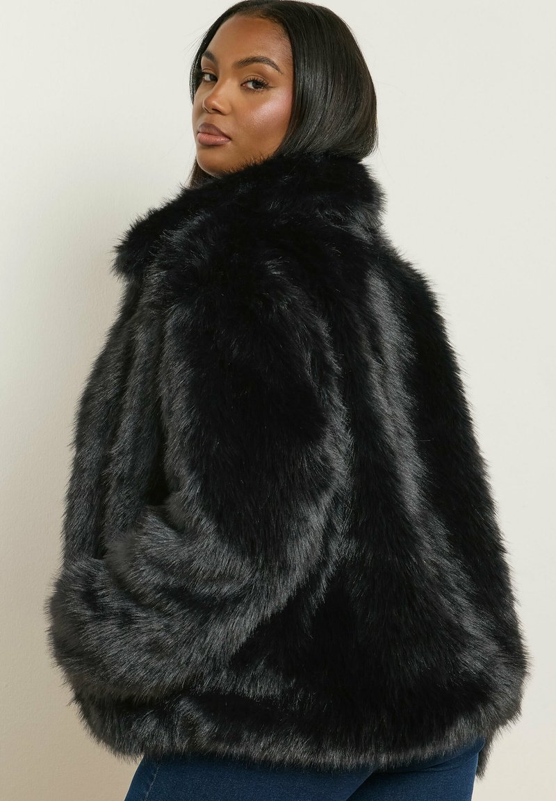Svart jacka i fuskpäls med en lös passform, hög krage och mjuk textur, med långa ärmar och en något cropped längd.