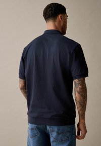 Marine polo shirt med korte ærmer, tekstureret stof og en klassisk krave. Sammen med blå jeans, der har en subtil denimvask.