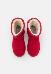 Bottines en daim rouge avec une douce doublure en shearling blanc et des détails en coutures. Bout rond et semelle plate et flexible.